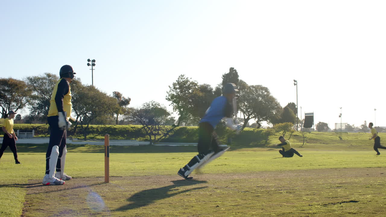 Cricket players in action on sunny field, batsman running between wickets