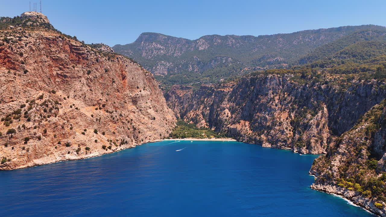 Stunning coastal view of a serene bay. A breathtaking coastal vista featuring clear blue waters, sandy beach, and surrounding rugged cliffs under a clear sky