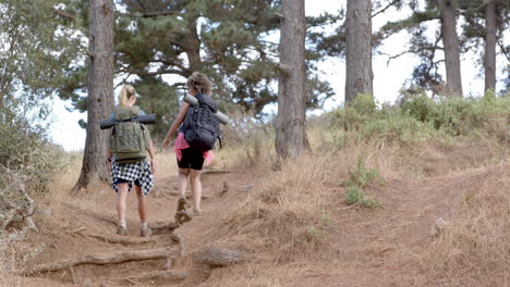 two women hike on a rugged trail amidst trees and dry grass with copy space