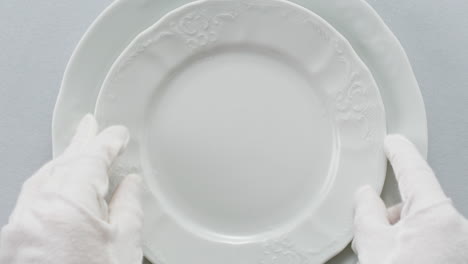 professional table setting with white gloves. plates, fork, knife, and glass arranged on a white table.