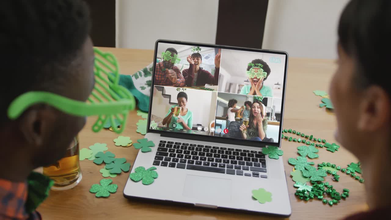 Smiling diverse group of friends with beer wearing clover shape items on video call on laptop