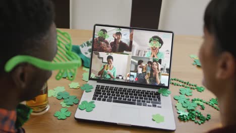 Smiling-diverse-group-of-friends-with-beer-wearing-clover-shape-items-on-video-call-on-laptop