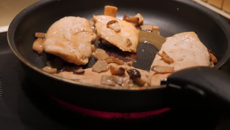 chicken with mushrooms in a frying pan on the stove - close up