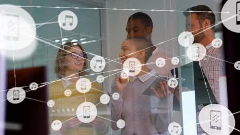 Network-of-digital-icons-against-diverse-office-colleagues-discussing-over-glass-board-at-office