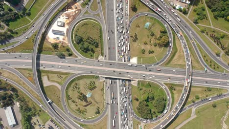 zoom en la toma de la intersección con pasos elevados y salidas de trébol. vista aérea de arriba hacia abajo desde el avión no tripulado. directamente por encima del punto de interés. zoom en el atasco de tráfico. soleado y seco. plantaciones de vegetación a su alrededor. la cámara se mueve hacia abajo.