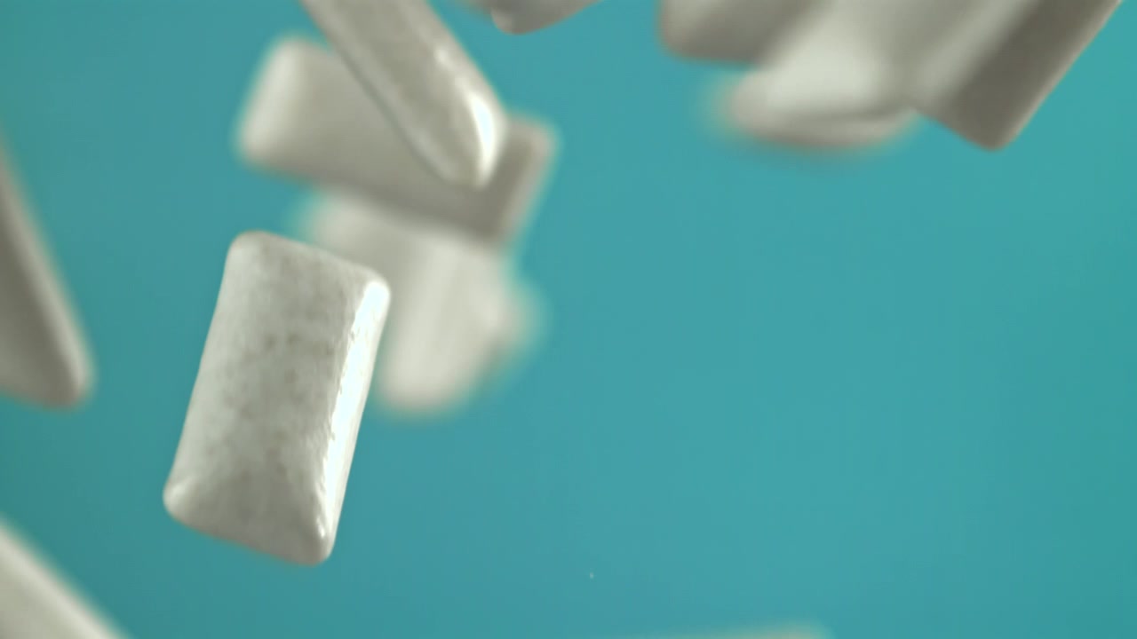 Pezzi di gomma da masticare bianca che cadono al rallentatore su sfondo blu.
