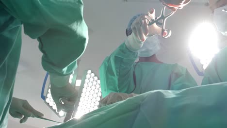 diverse surgeons wearing surgical gowns operating on patient in operating theatre, slow motion