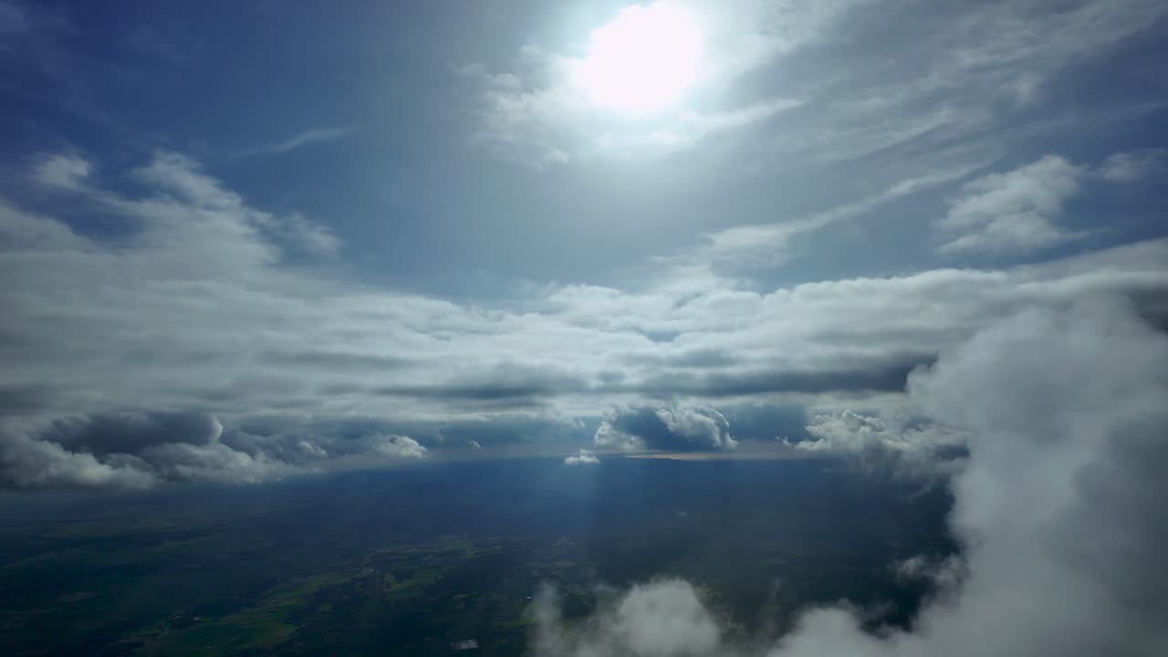 La prospettiva di un pilota catturata dalla cabina di pilotaggio di un jet che vola attraverso una piccola nuvola cumuliforme ed emerge in un cielo limpido e luminoso con un sole radioso in alto in un cielo azzurro