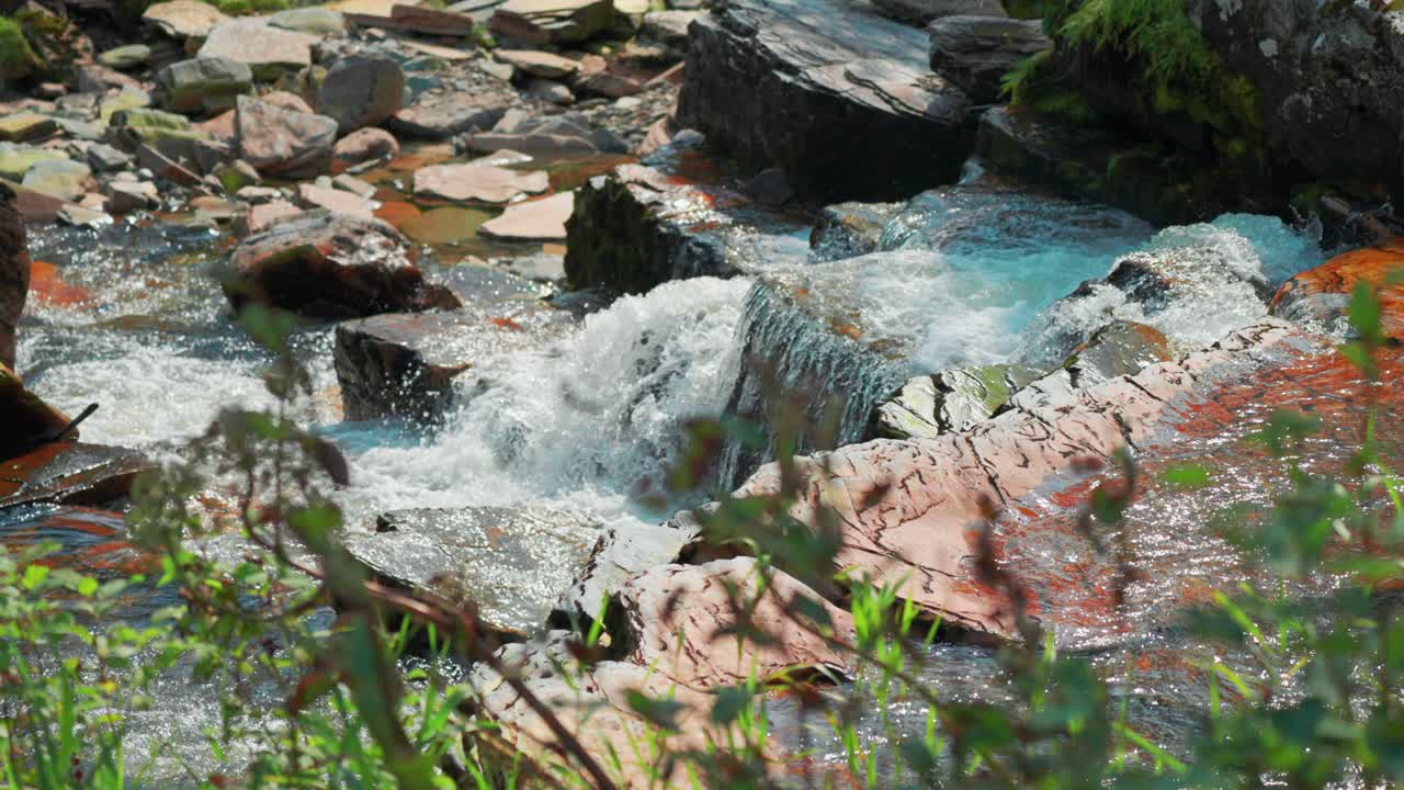 A picturesque waterfall cascades over withered rocks, with water sparkling in the sunlight and vibrant green foliage creating a tranquil scene