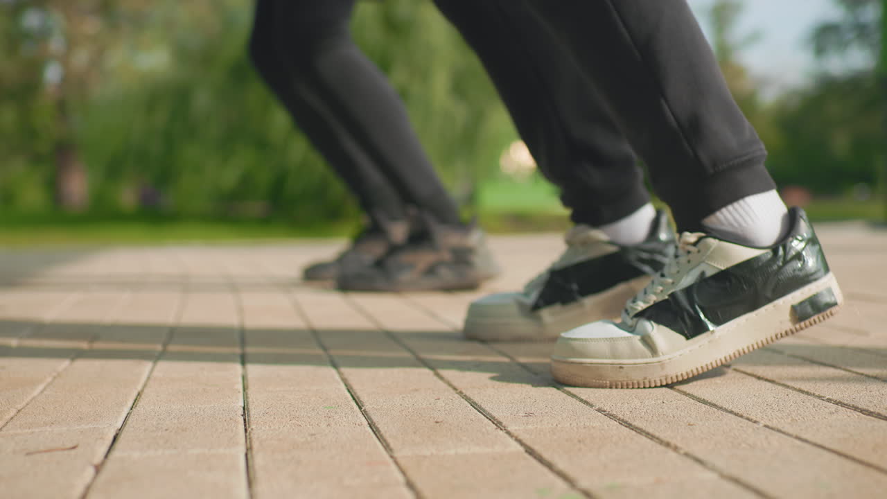 close up sneakers tapping on pavement during park rehearsal, two dancers practicing quick rhythmic footwork, worn white sneakers, textured tiles, warm sunlight, casual streetwear vibe, energetic