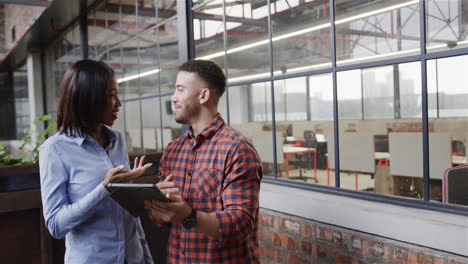 Diverse-male-and-female-colleagues-standing,-talking,-smiling,-looking-at-tablet-and-camera