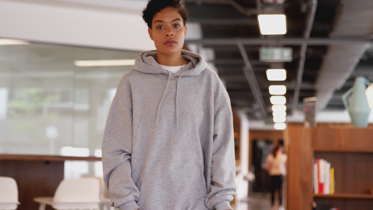 캐주얼 옷을 입은 젊은 사업가 여성이 오픈 플랜 작업장에서 스케이트보드를 타고 있습니다.