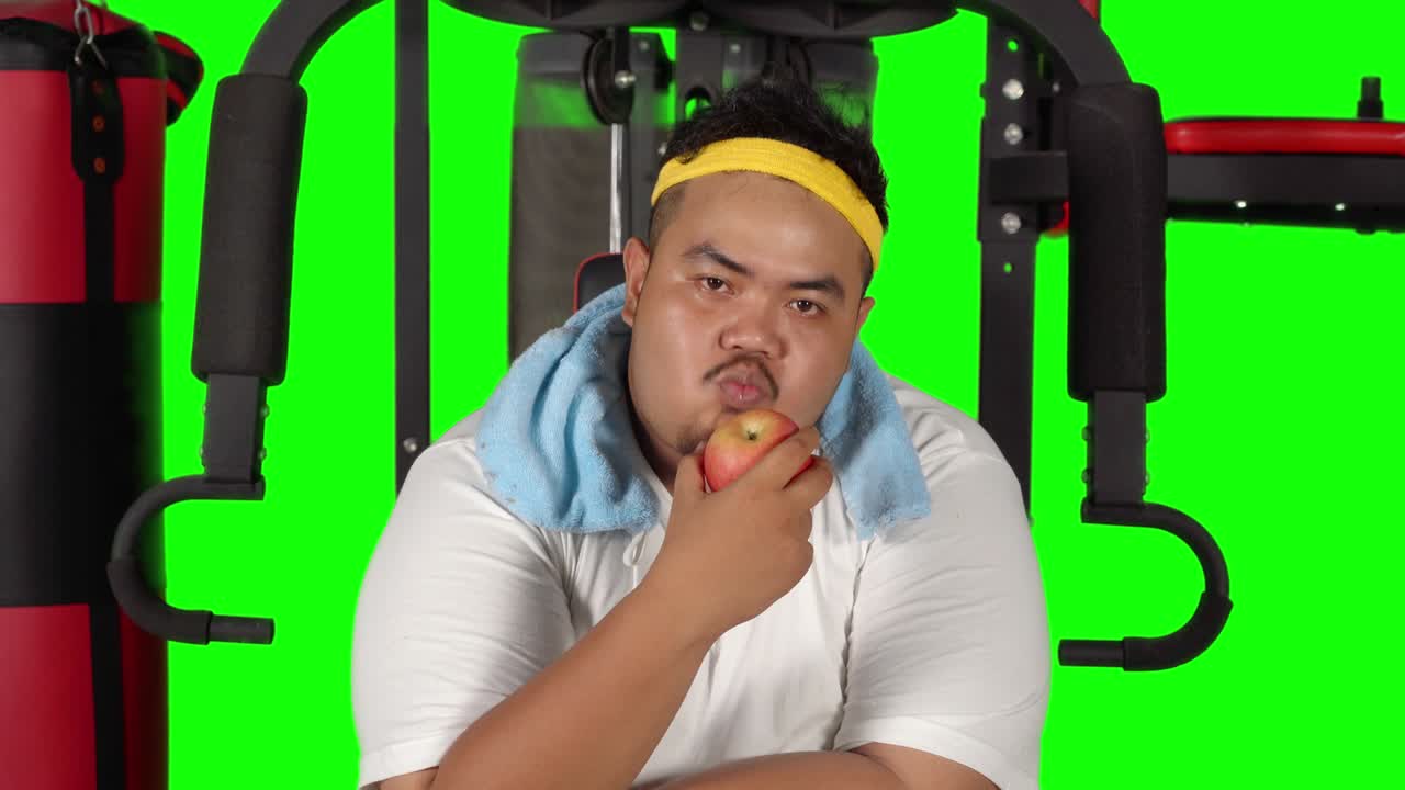 Overweight man eating apple on gym machine