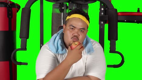 overweight man eating apple on gym machine