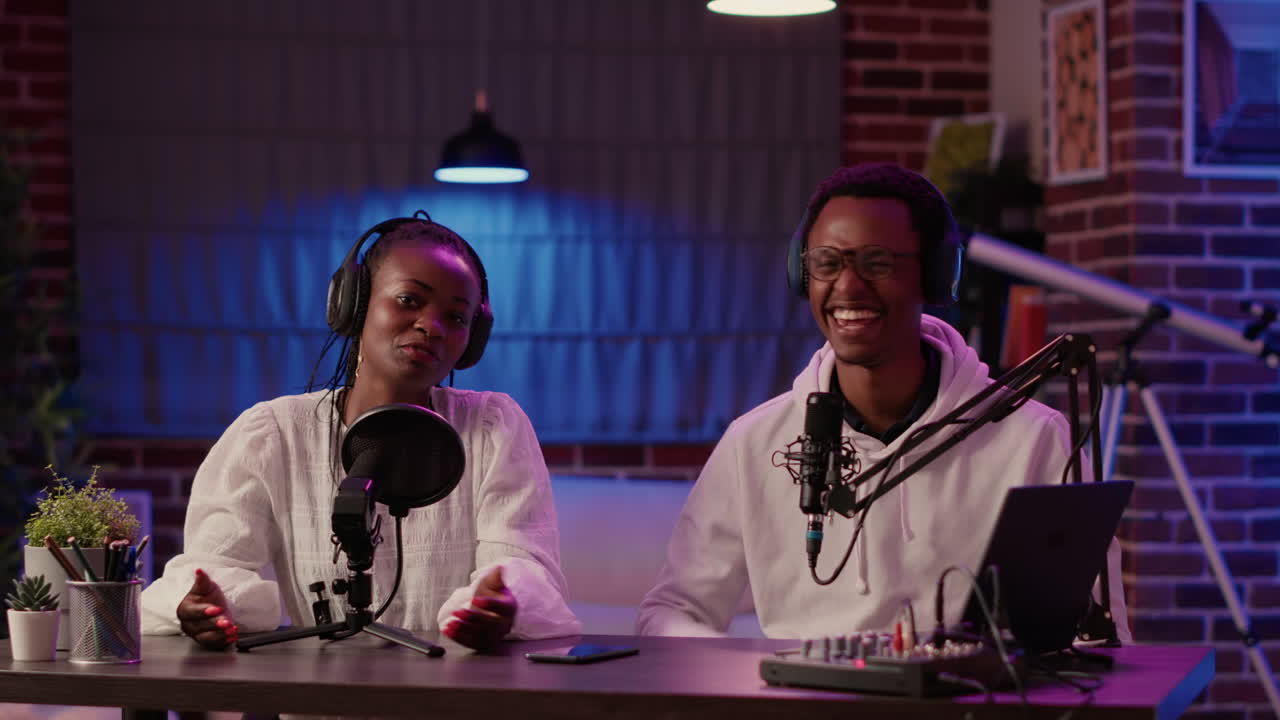 African american influencer couple streaming live dual vlog talking sitting at desk with podcast setup