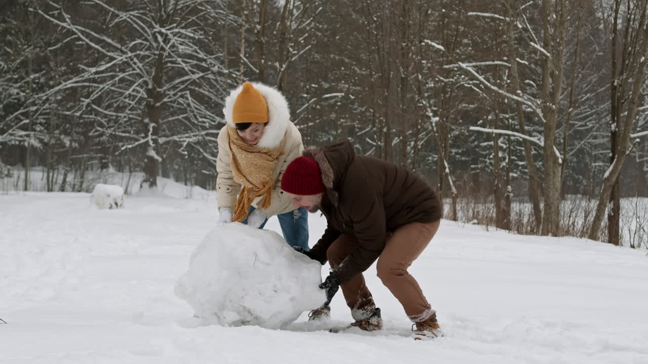 pareja haciendo un muñeco de nieve en la nieve