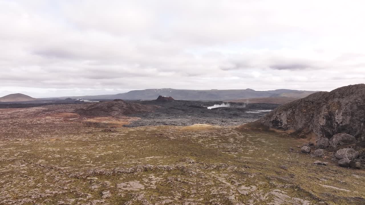 Wide aerial view of an Icelandic volcanic landscape with steaming vents and rugged terrain under a cloudy sky