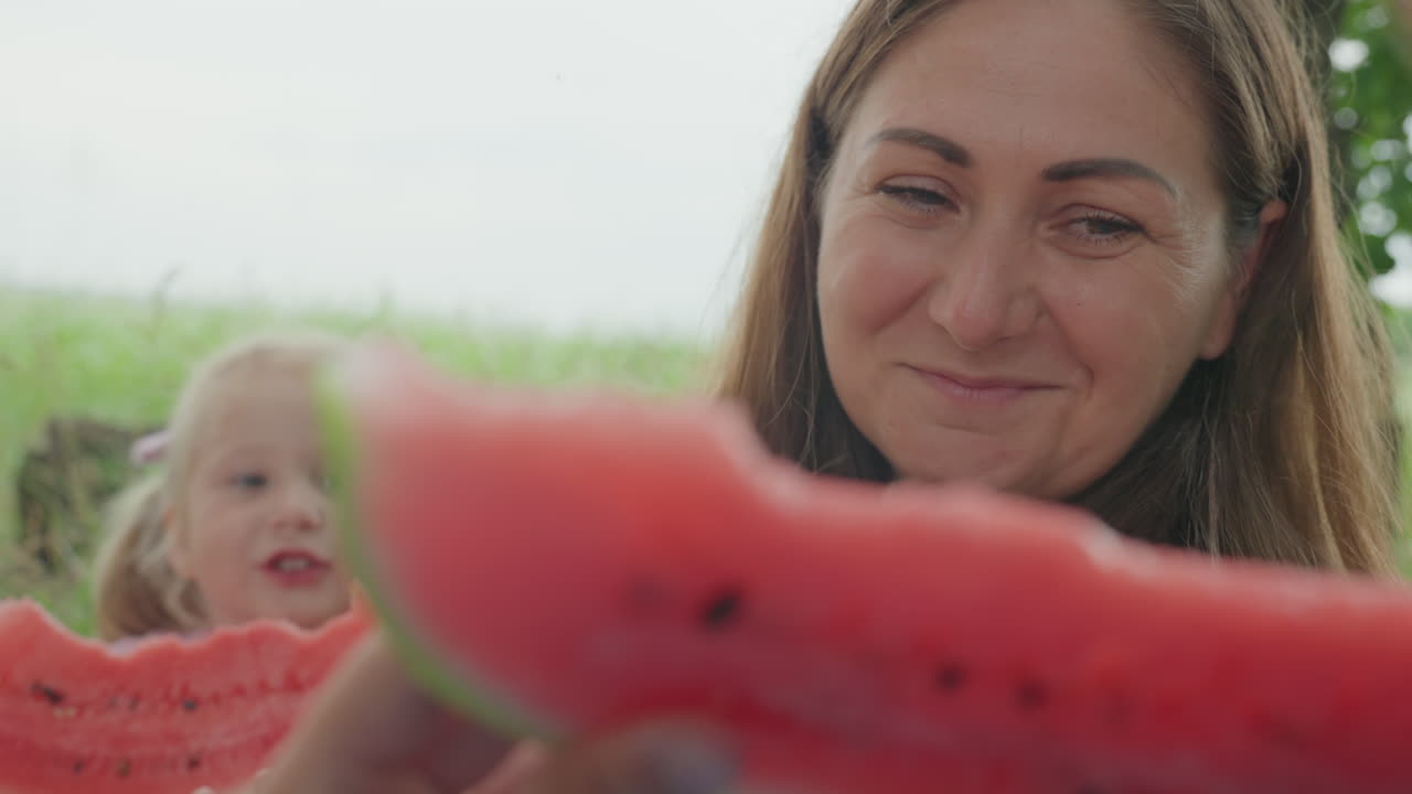Family summer bonding, Caucasian mother and daughter sharing slices in tranquil summer setting, Seaside meadow backdrop as family members exchange watermelon slices in warm summer atmosphere