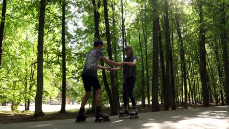 young couple learning how to skate with roller blades in the park, holding hands, slow motion