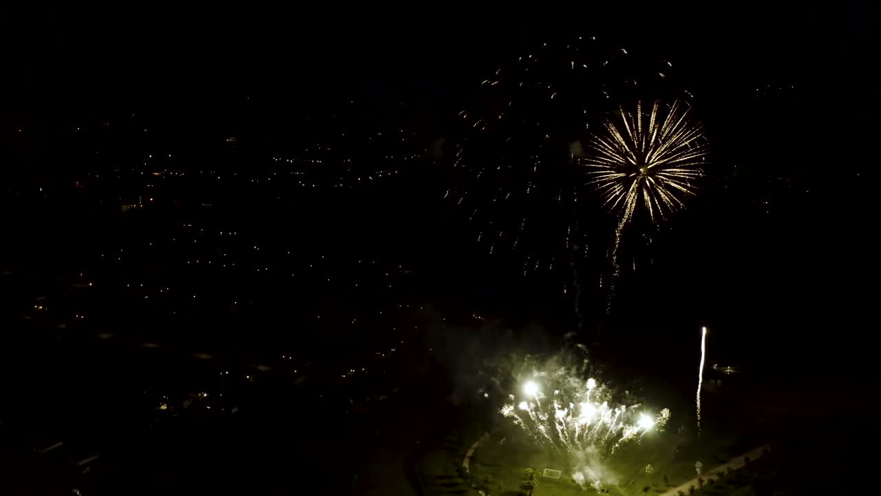 toma aérea de fuegos artificiales con luces de la ciudad en el fondo