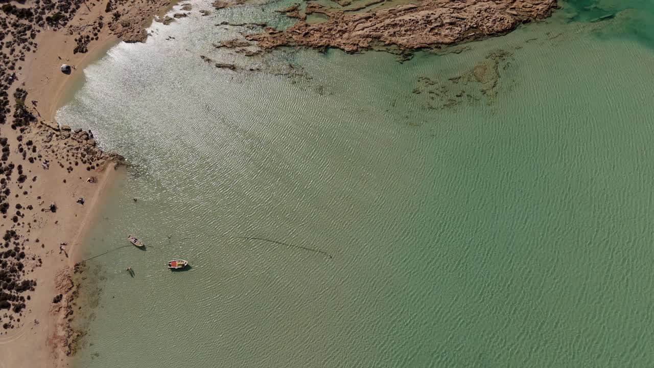 Aerial - two small boats in turquoise shallow waters near a sandy beach in Crete Greece