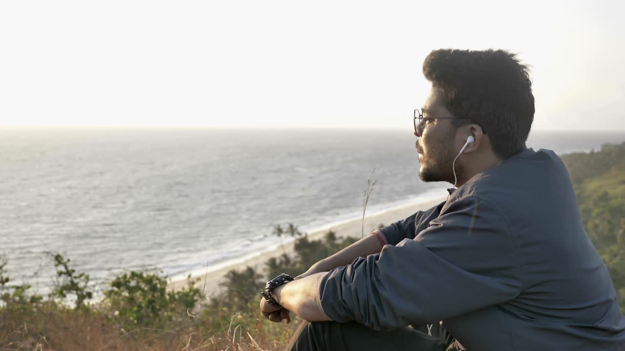 joven viajero o turista con chaqueta y gafas sentado en la cima de una montaña