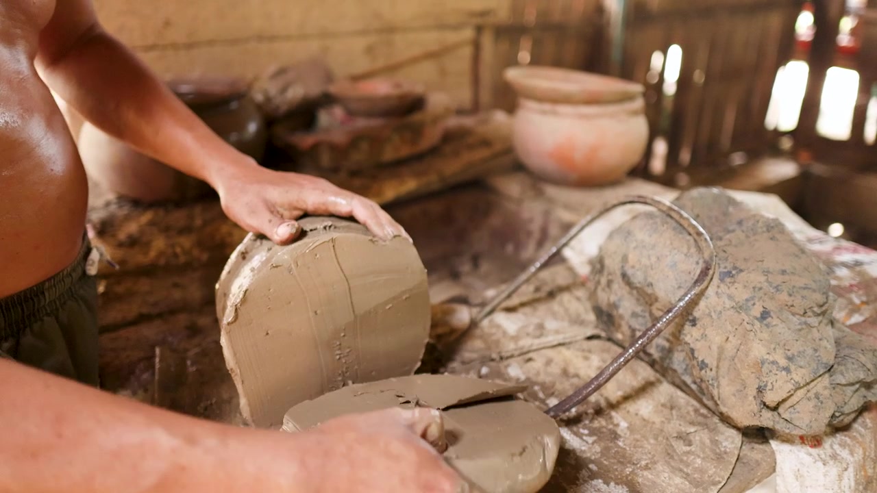 Primo piano delle mani di un artigiano che tagliano argilla umida con uno strumento a filo in un rustico studio di ceramica