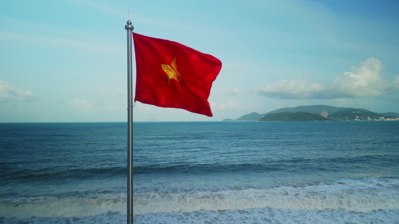 Bandera de Vietnam ondeando en playa con océano y montañas