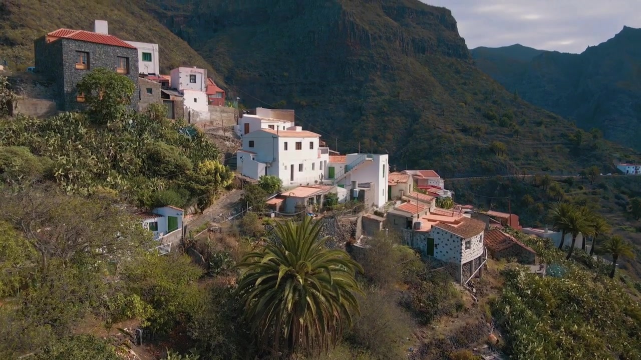 Dolly aéreo panorâmico de uma vila montanhosa coberta por vegetação, ao anoitecer