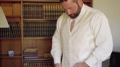 revelación en cámara lenta del novio barbudo ajustando su elegante chaleco blanco y corbata rosa el día de la boda