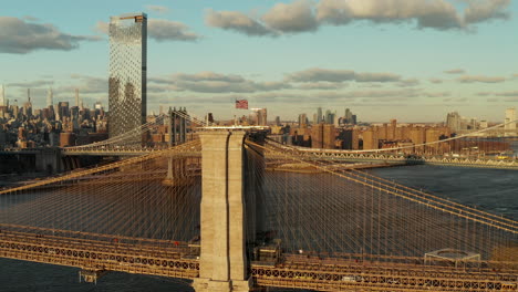 American-flag-on-top-of-Brooklyn-Bridge.-Picturesque-aerial-footage-of-bridges-and-buildings-in-city-illuminated-by-setting-sun.-Manhattan,-New-York-City,-USA