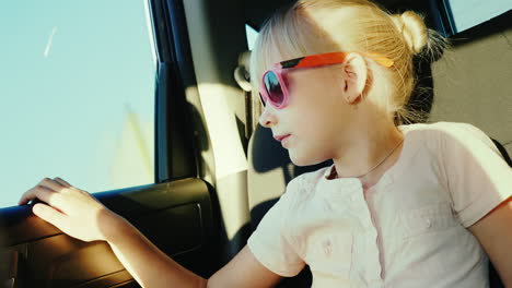 a 6-year-old girl in sun-protective pink glasses is riding in the back seat of the car it is fastene