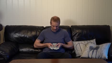 man in sofa with four $100 bills, expressing financial concern