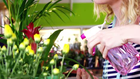 female florist spraying water on flowers in flower shop