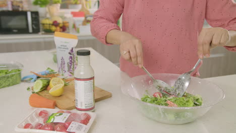 mid shot of woman finalizing her salad recipe and picking it up