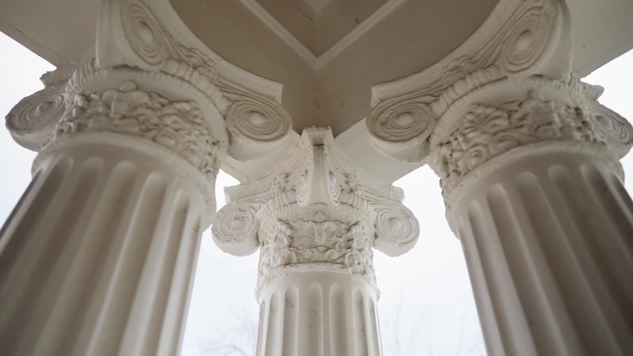 Upward view of ornate white Ionic columns with detailed capitals supporting a covered entry