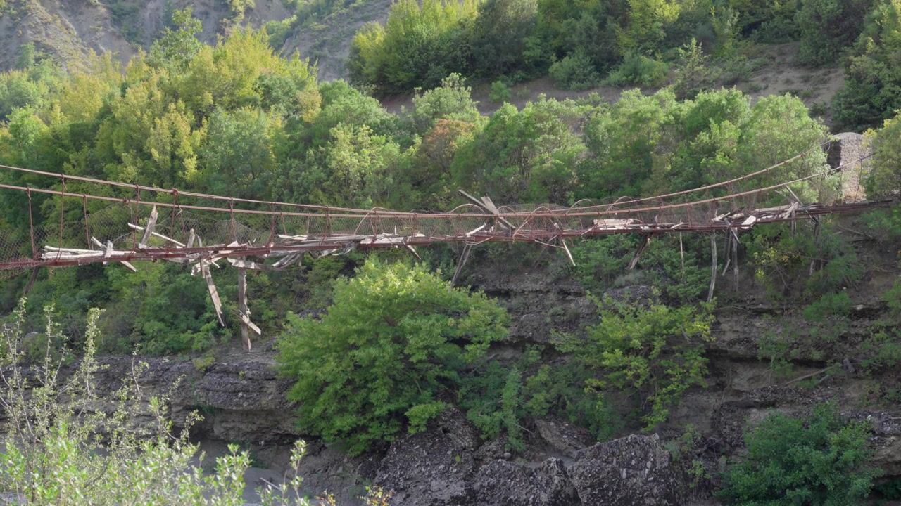 Pasarela colgante destruida a la que le faltan tablones de madera rotos y barandillas de metal oxidadas.