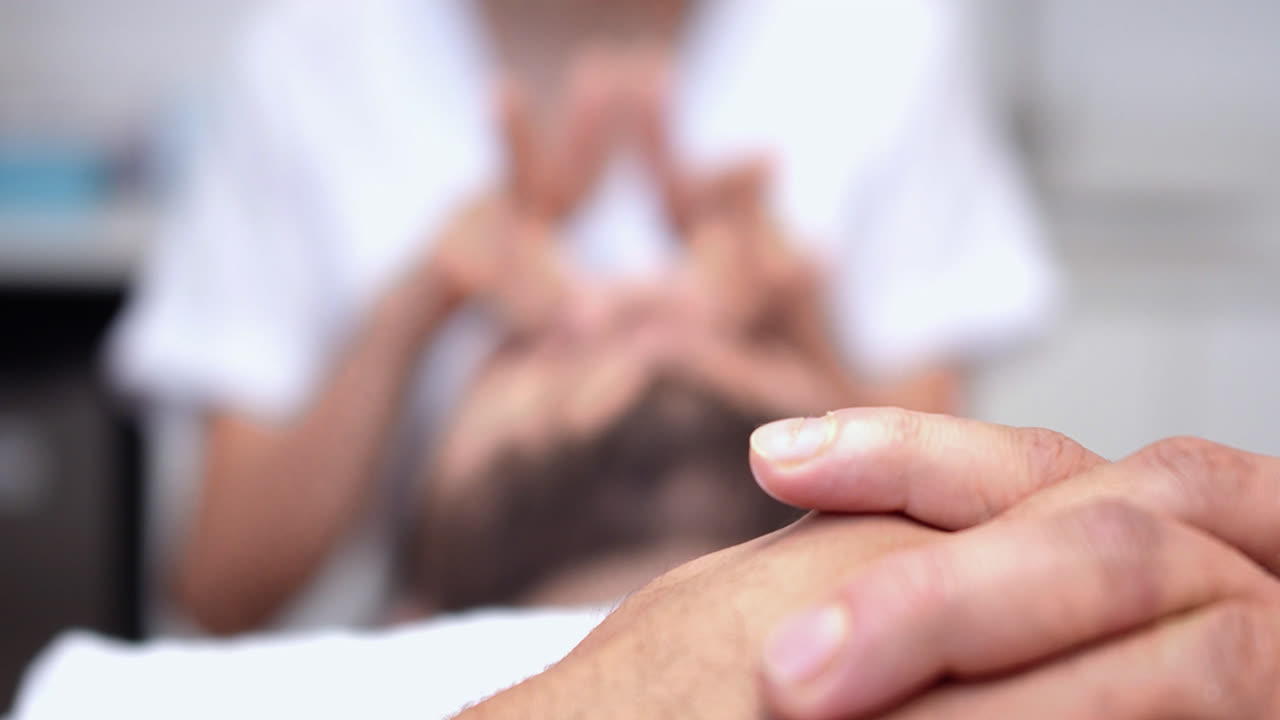 Beautiful slow motion shot from the hands of a young man lying on a stretcher receiving a beauty treatment by a young nurse in a dermatology clinic.