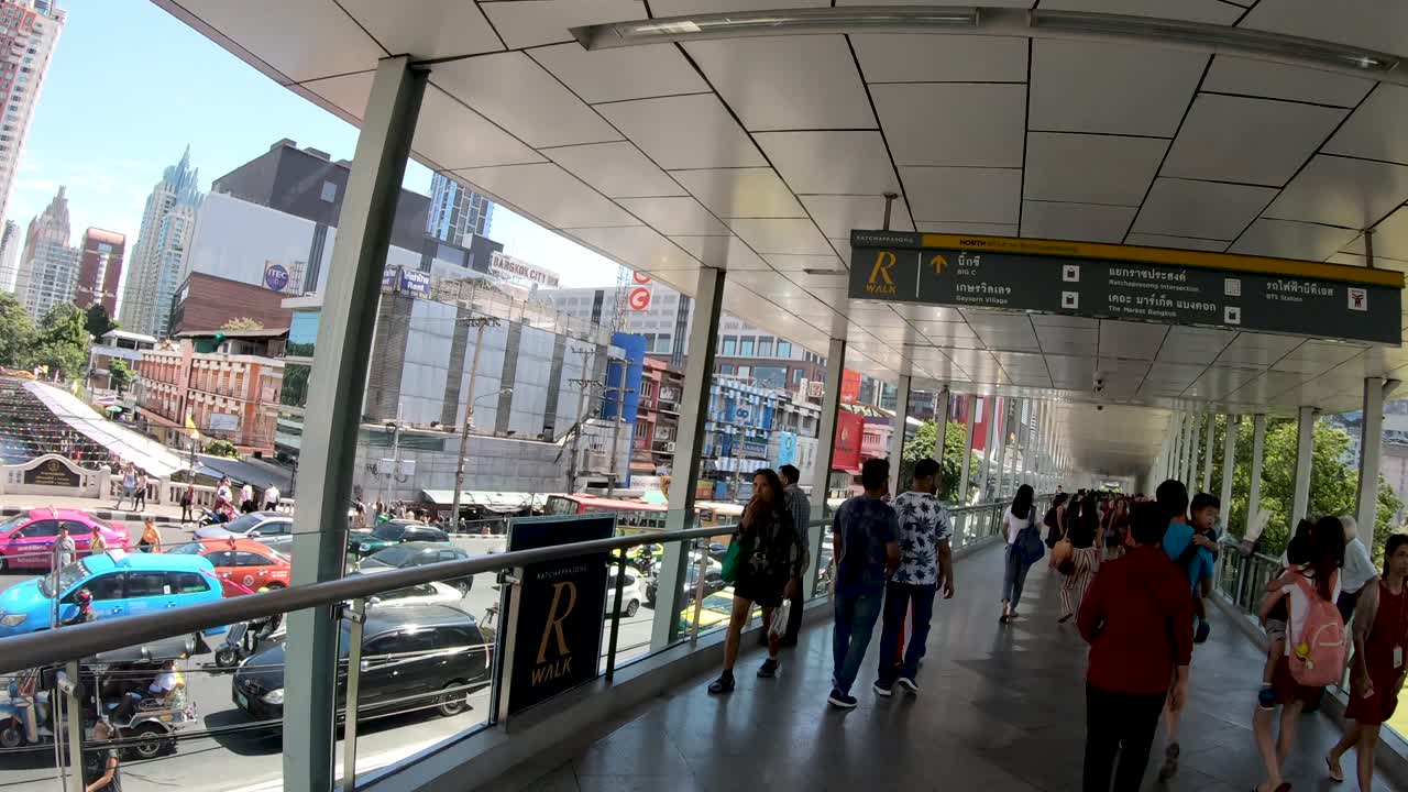 People walking on Ratchaprasong SkyWalk, aka R Walk, and heavy street traffic at Ratchadamri street on a sunny day.