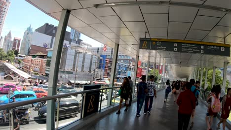 people walking on ratchaprasong skywalk, aka r walk, and heavy street traffic at ratchadamri street on a sunny day.