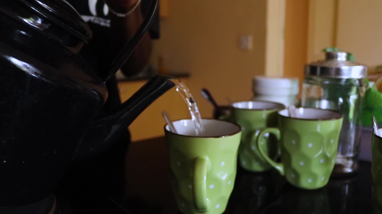 Close up shot of a person pouring out water into the glass cups from a teapot at breakfast on the table at Harare, Zimbabwe.