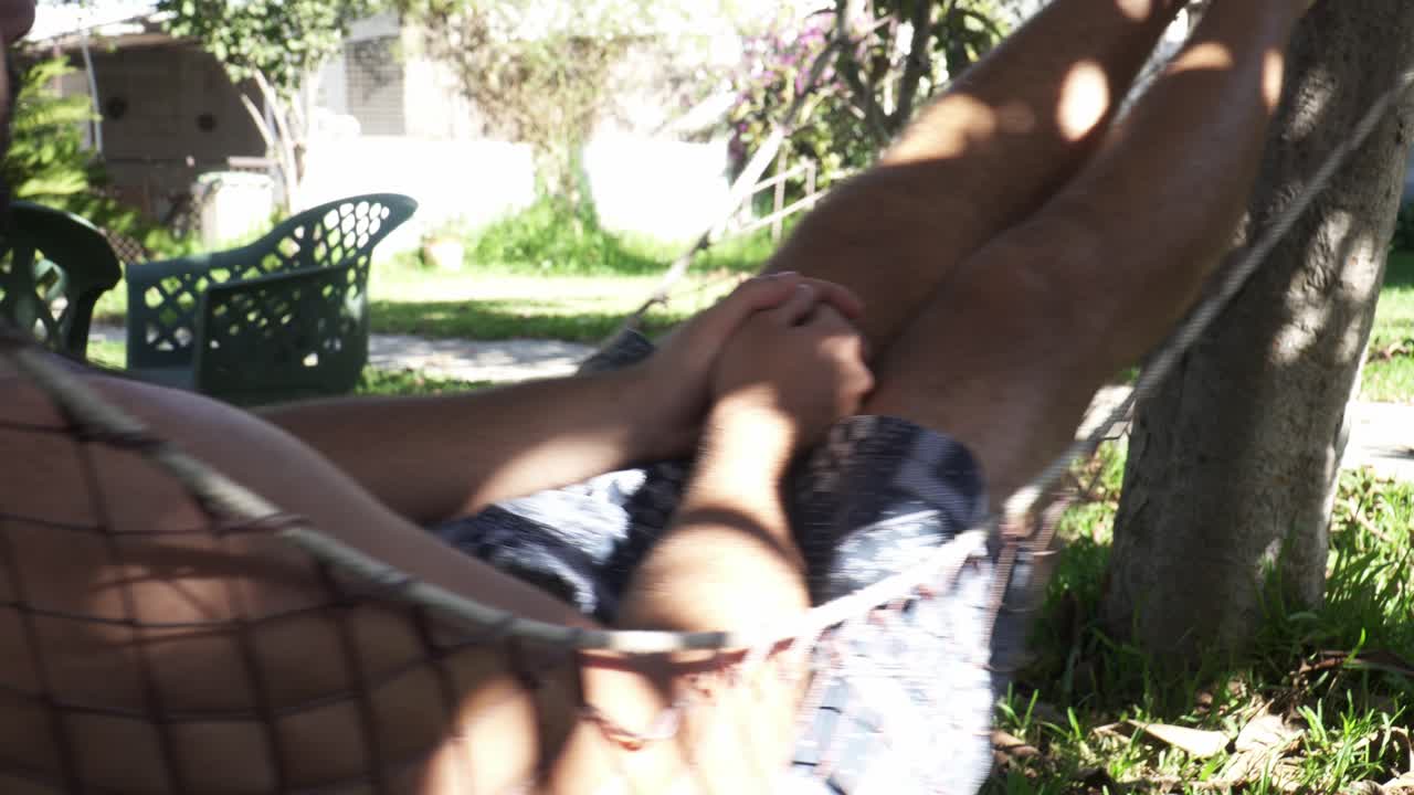 chico guapo relajándose y columpiándose en una hamaca de vacaciones afuera en un día soleado