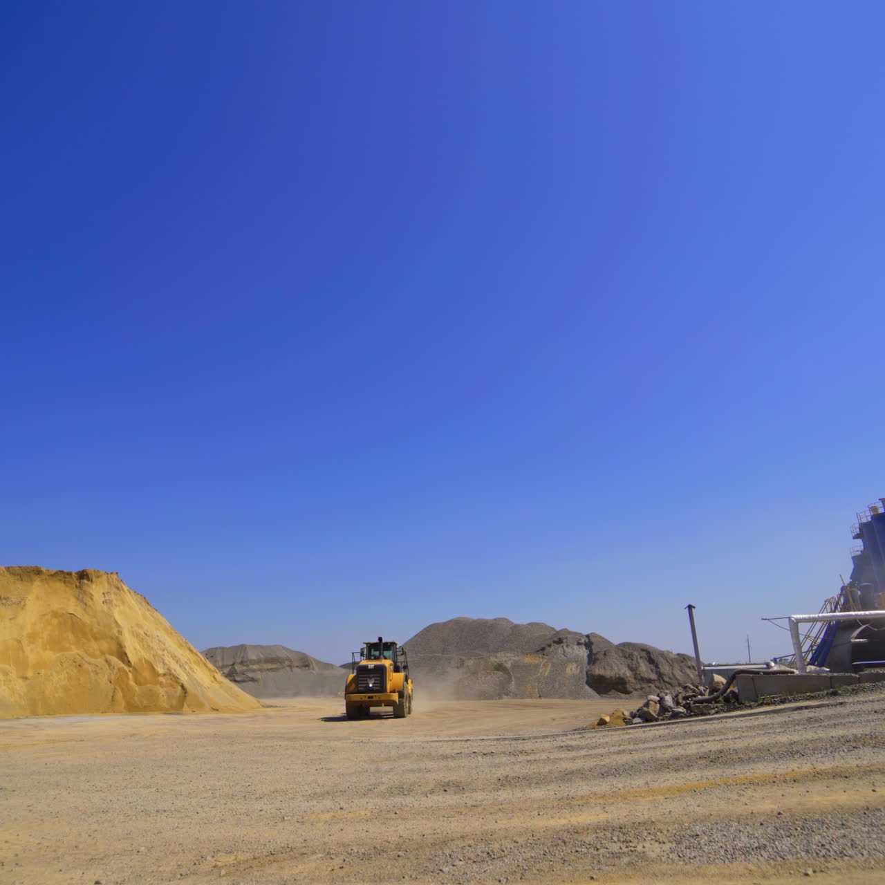Asphalt manufacturing plant outdoors. Excavator working . Piles of sand on the environmental background.