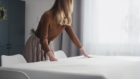 una mujer caucásica colocando la mesa con un mantel blanco.