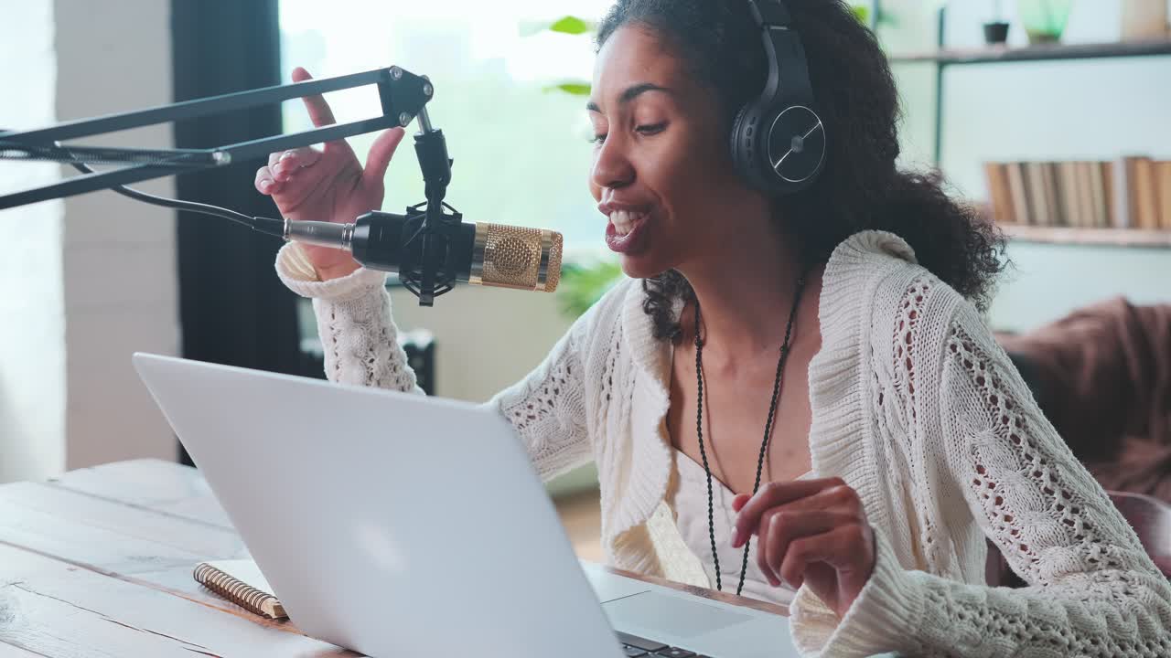 Young charismatic african american woman sits at desk with microphone and laptop