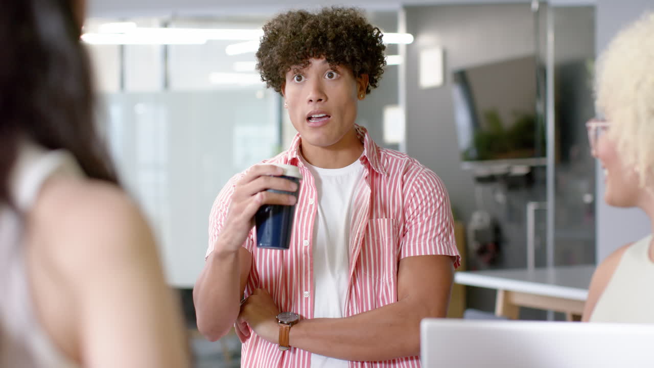 Holding coffee cup, man engaging in conversation with colleagues in office