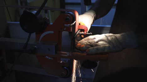 man using protective glove sanding a knife using a sanding machine creating beautiful and energetic red sparks with small camera movement