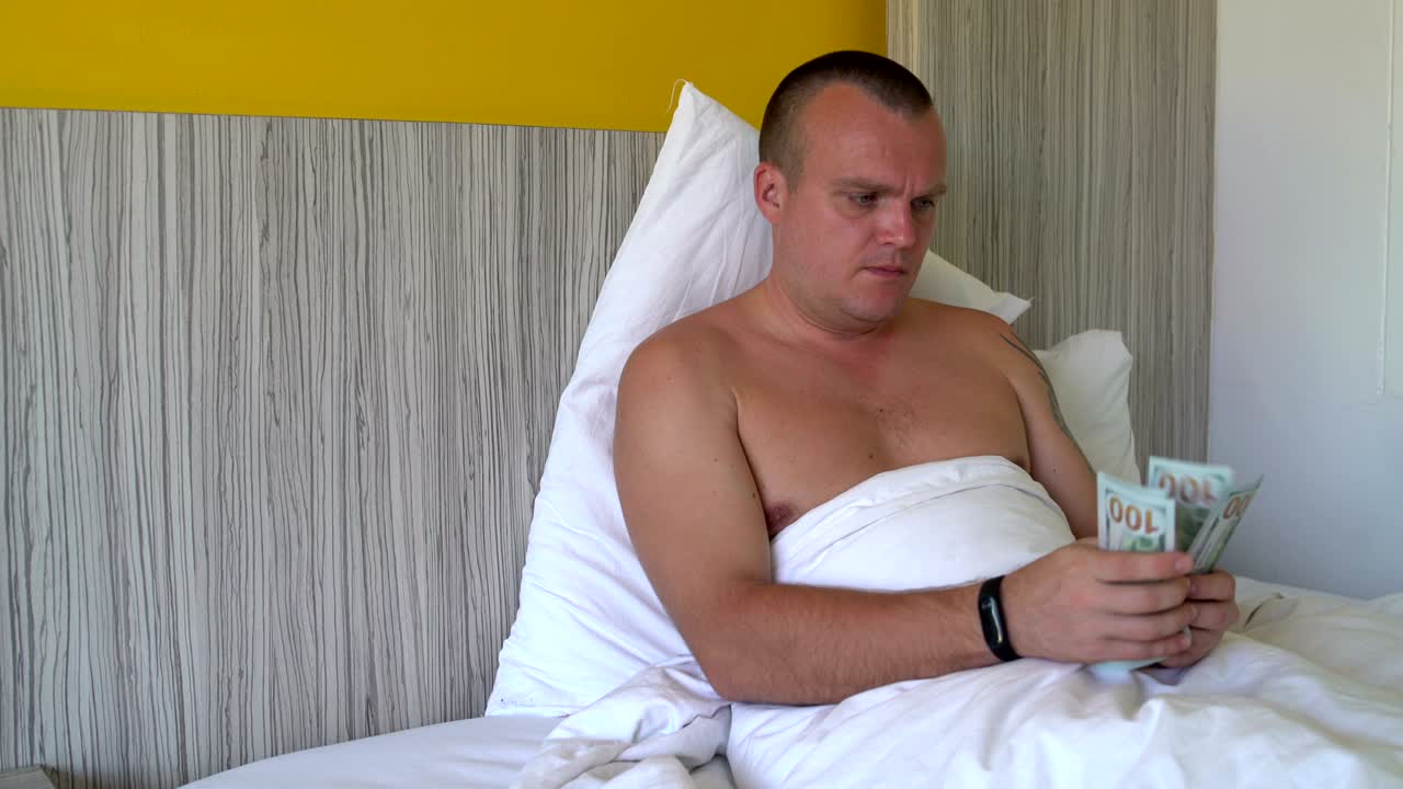 A man is lying in bed and counting money and giving them away.