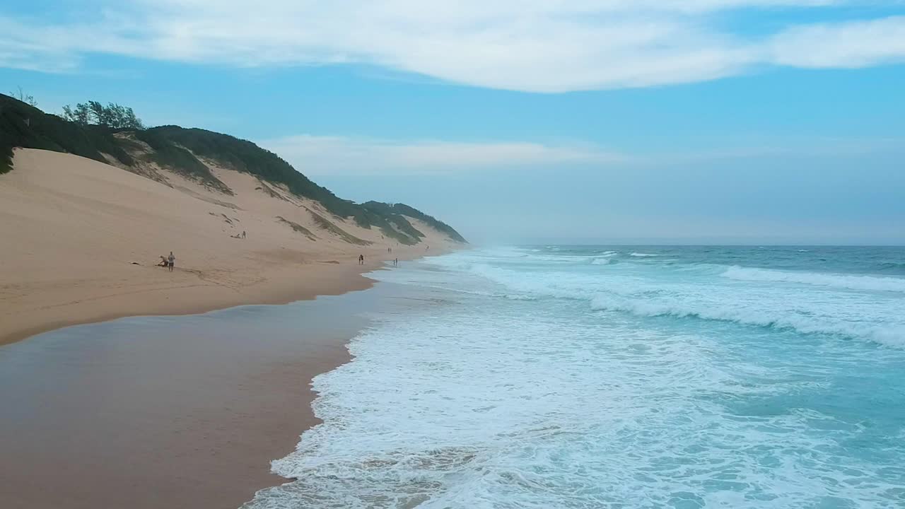 vista aérea de bajo vuelo de olas azules y playa en mozambique, gente caminando en la playa