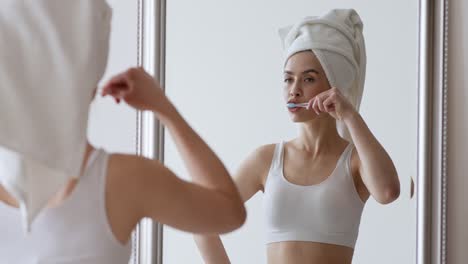 woman brushing teeth in front of mirror